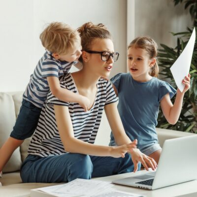 Tired,Young,Mother,Sitting,On,Sofa,And,Working,With,Laptop